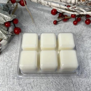 Picture of 6 wax melt cubes laying upside down featuring the white cubes. Container is laying beside Christmas tree and berries